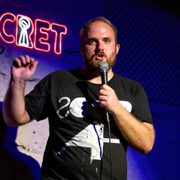 Jake Graves on stage with a microphone, mid rant